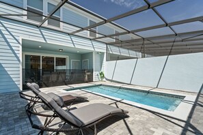 A pool area with two lounge chairs, a glass-enclosed patio, and a clear blue sky. - 5BR Home w/ Private Pool & Themed Rooms (Clermont)