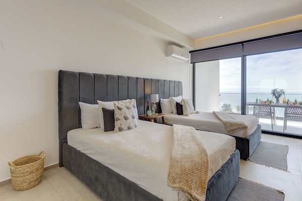 Et moderne hotelværelse med en stor seng, en mindre seng, en balkon med udsigt og en flettet kurv.
