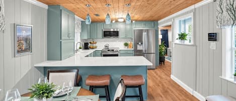 A modern kitchen with a central island, wooden ceiling, and light blue cabinetry.