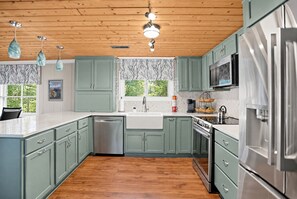 Una cocina moderna con gabinetes verdes, electrodomésticos de acero inoxidable y techo de madera.