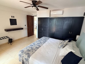 A bedroom with a bed, a ceiling fan, a wardrobe, a mounted TV, and a wall-mounted air conditioner. - Beautiful BEACHFRONT apartment for 4 people with a spectacular view. (Zihuatanejo)