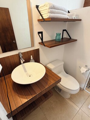 A bathroom with a wooden vanity, a white sink, a toilet, and a towel rack with towels. - Beautiful BEACHFRONT apartment for 4 people with a spectacular view. (Zihuatanejo)