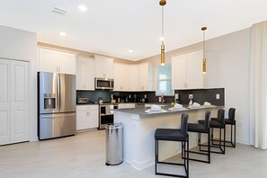 Une cuisine moderne avec des meubles blancs, des appareils en acier inoxydable et un îlot central doté de tabourets de bar.