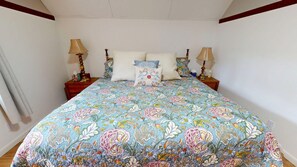 Une chambre à coucher avec une couvre-lit à motifs floraux, deux tables de chevet avec des lampes et une petite table de nuit avec une lampe.