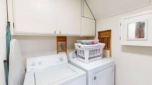 Un espace buanderie comprenant un lave-linge et un sèche-linge, un panier à linge et une étagère en bois avec des serviettes pliées.