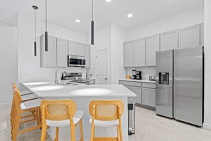 A modern kitchen with white cabinets, stainless steel appliances, and a central island with seating. - Luxury 5suite Home Near Epic Universe (Orlando)