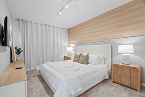 A modern hotel room with a large bed, white bedding, a wooden headboard, bedside lamps, a flat-screen TV, and a small plant on a wooden desk. - Luxury 5suite Home Near Epic Universe (Orlando)