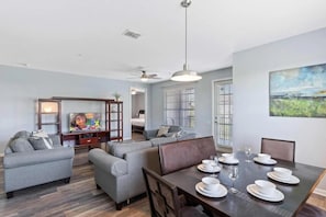 Un salon moderne avec un coin repas, des canapés gris, un téléviseur à écran plat et un tableau accroché au mur.