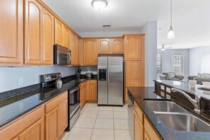 A kitchen with wooden cabinets, a stainless steel refrigerator, and a black countertop. - Elegant 4BR Vista Cay Resort (Orlando)