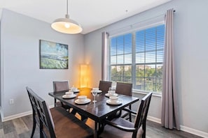Un coin repas avec une table dressée pour quatre personnes, un luminaire suspendu et une grande fenêtre avec des rideaux.