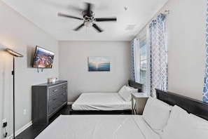A bedroom with two beds, a ceiling fan, a TV, a painting, and patterned curtains. - Modern Multi-story 3BR Condo at Vista Cay (Orlando)