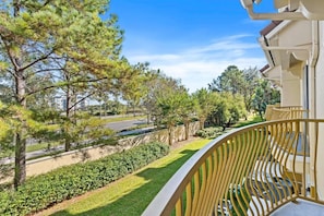 A balcony with a curved railing overlooking a landscaped garden with trees and a road. - Modern Multi-story 3BR Condo at Vista Cay (Orlando)