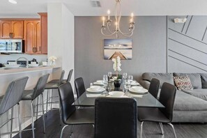 A modern dining area with a glass table, black chairs, and a chandelier. - Modern Multi-story 3BR Condo at Vista Cay (Orlando)
