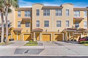 A multi-story residential building with a yellow facade, multiple garage doors, and a paved driveway. - Modern Multi-story 3BR Condo at Vista Cay (Orlando)
