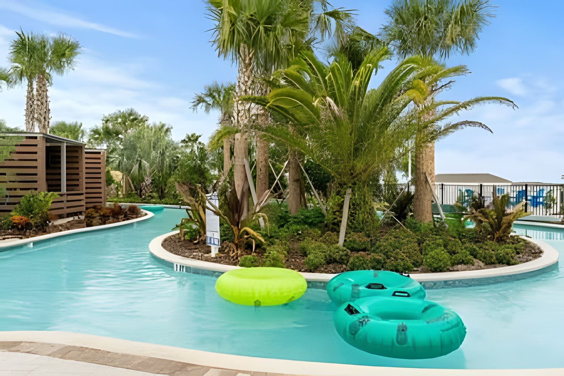 Une piscine avec des bouées gonflables, entourée de palmiers et d’une structure en bois.