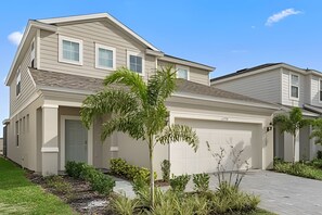 A two-story residential building with a garage, a driveway, and a well-maintained garden with various plants. - Luxury 5BR Villa Near Disney w/ Lazy River Access (Davenport)
