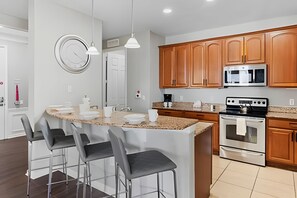 A modern kitchen with wooden cabinets, a stainless steel microwave, and a gas stove. - Vista Cay 4BR Condo w/ Balcony & Foosball Fun (Orlando)