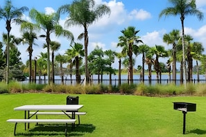 A picnic table and mailbox in a grassy area with a lake and tall trees in the background. - Vista Cay 4BR Condo w/ Balcony & Foosball Fun (Orlando)
