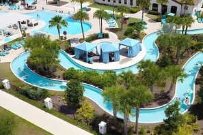 A large, multi-lane swimming pool with a winding design, surrounded by palm trees and shaded areas. - Windsor 5BR Villa w/ Pool Near Disney (Kissimmee)