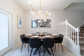 A dining area with a round table, black chairs, a chandelier, and a staircase with white railings. - Windsor 5BR Villa w/ Pool Near Disney (Kissimmee)