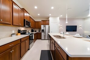A modern kitchen with wooden cabinets, stainless steel appliances, a large island with a sink, and recessed ceiling lighting. - Windsor 5BR Villa w/ Pool Near Disney (Kissimmee)