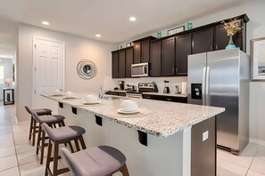 A modern kitchen with a large island, dark cabinets, stainless steel appliances, and a white door. - Modern 6BR Villa w/ Pool & Resort Access (Kissimmee)