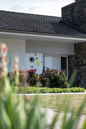 A building with a tiled roof, a white facade, and a stone wall. There is a door with a sign above it, and a small window on the wall. - A 5-star single-story vacation home with all the comforts and a large garden. (Poperinge)