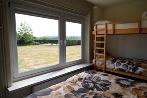 A room with two bunk beds, a window with a view of a grassy area, and a radiator below the window. - A 5-star single-story vacation home with all the comforts and a large garden. (Poperinge)