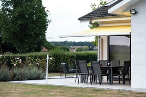 An outdoor patio with a table and chairs, a yellow awning, and a view of the countryside. - A 5-star single-story vacation home with all the comforts and a large garden. (Poperinge)