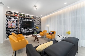 Una sala de estar moderna con una pared estampada en blanco y negro, un televisor de pantalla plana, sofás amarillos y negros y una mesa de centro.