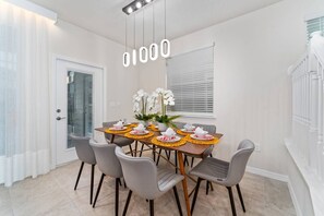 Un comedor con una mesa dispuesta para seis personas, seis sillas grises y un jarrón con flores blancas.