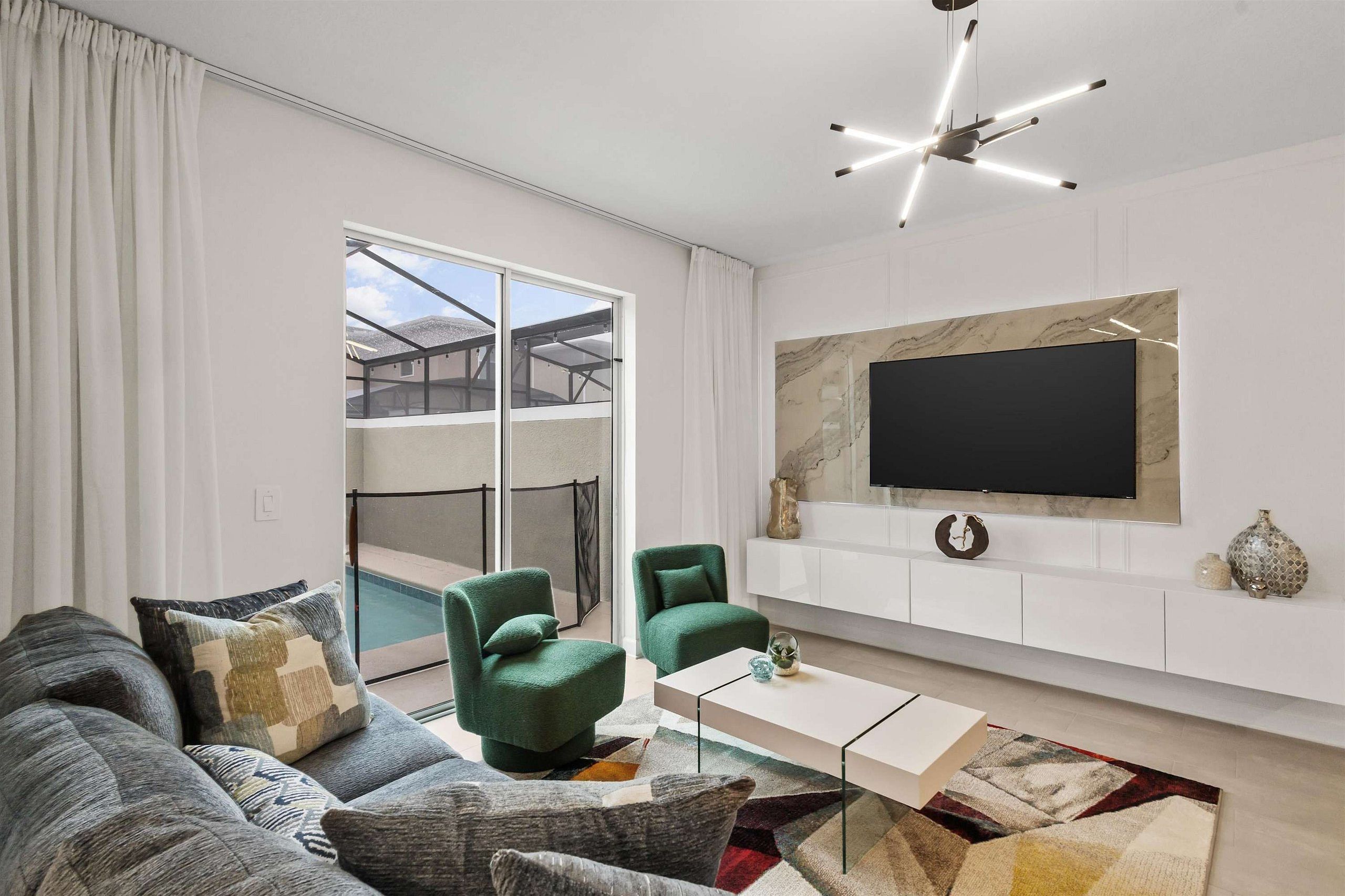 Una sala de estar moderna con un sofá, dos sillones, una mesa de centro y un televisor de pantalla plana montado sobre una pared de mármol.