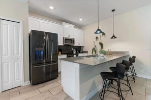 A modern kitchen with white cabinetry, stainless steel appliances, a large island with bar stools, and pendant lighting. - 5BR Storey Lake Pool Home Near Disney (Kissimmee)