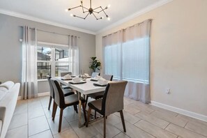 A dining area with a table set for four, a sofa, and a window with curtains. - 5BR Storey Lake Pool Home Near Disney (Kissimmee)