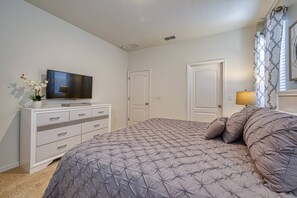 A bedroom with a bed, a TV on a dresser, and two doors. - 6br/6ba Private Pool Home in Solterra (Davenport)
