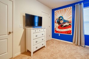 A room with a white dresser, a television on top, a blue wall with a superhero mural, and beige carpet. - 6br/6ba Private Pool Home in Solterra (Davenport)