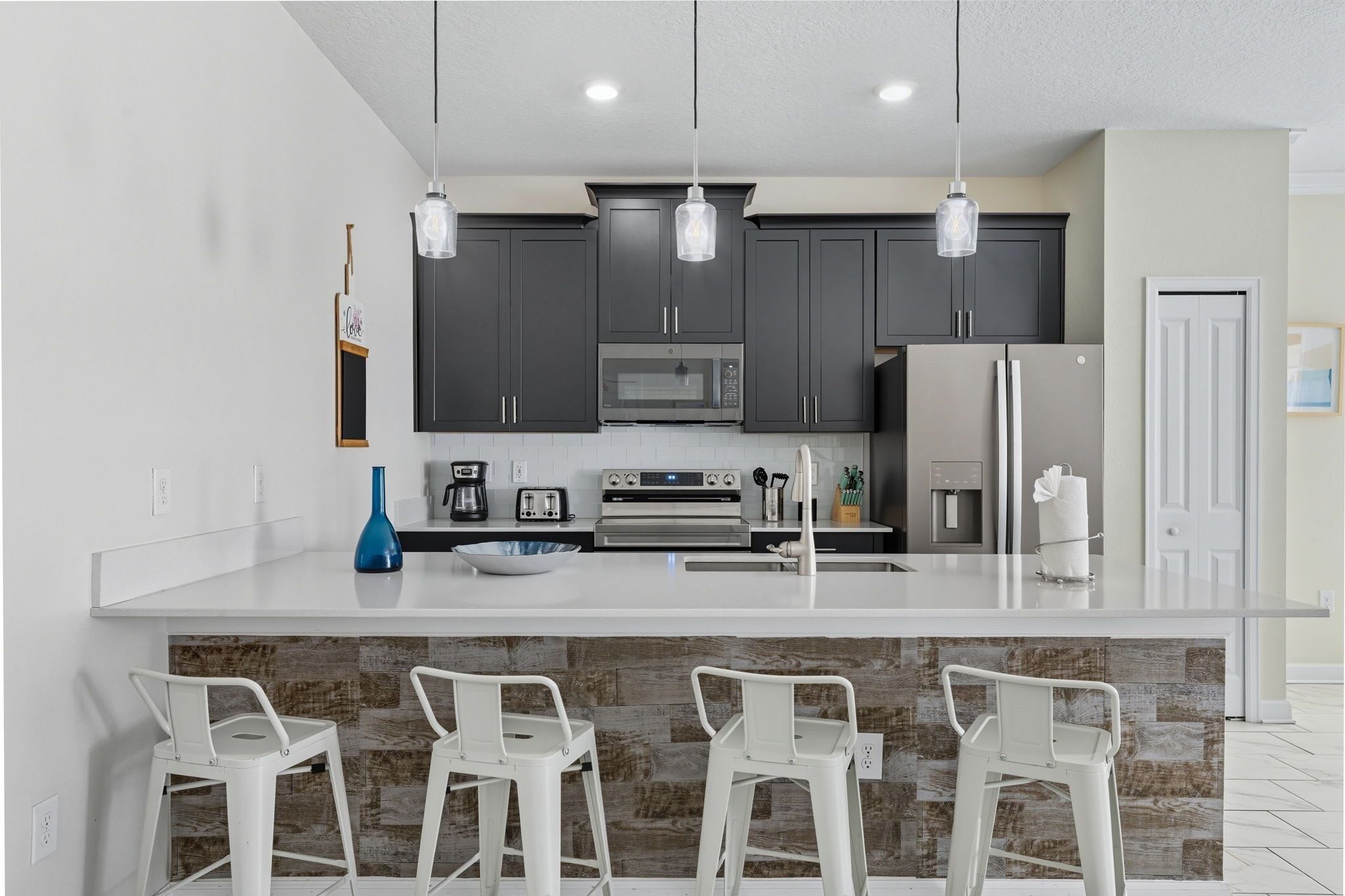 Una cocina moderna con armarios oscuros, una isla grande con taburetes de bar, un microondas y un refrigerador.