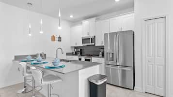 Una cocina moderna con gabinetes blancos, electrodomésticos de acero inoxidable y una isla central con taburetes de bar.