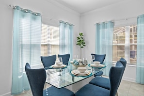 A dining area with a glass table, blue chairs, and a plant. - 5BR Townhome w/ Pool at Champions Gate (Davenport)