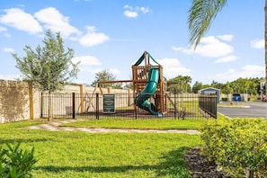 A playground with a slide and climbing structure, surrounded by a fence and greenery. - 4BR Family Townhome 15min to Disney (Kissimmee)