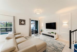 Ein modernes Wohnzimmer mit einer Couch, Fernseher und Blick ins Freie.