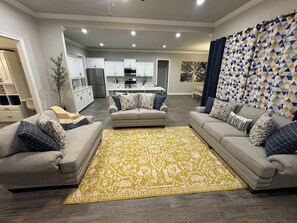 A modern living room with two sofas, a patterned rug, and a kitchen in the background. - Game Day Getaway / Near Sports Complex / Sleeps 10 / 4BR/3BA (Youngsville)