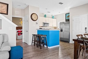 A modern kitchen with a blue island, stainless steel appliances, and a dining area with wooden furniture. - 4BR Resort Townhome 15 Min From Disney (Kissimmee)