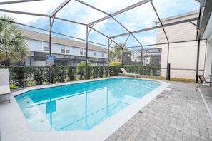 A swimming pool with a glass enclosure, surrounded by a paved patio and a hedge. - 5br/4ba Luxury Home Private Pool (Kissimmee)