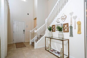 A hallway with a white door, a staircase, and a console table with decorative items. - 5br/4ba Luxury Home Private Pool (Kissimmee)