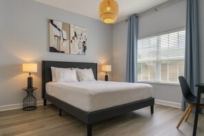A modern bedroom with a large bed, two bedside lamps, abstract wall art, and a window with curtains. - 5BR Storey Lake Home, Sleeps 13 (Kissimmee)