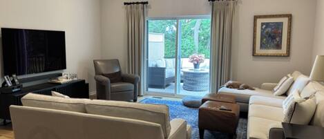 A modern living room with a sofa, armchairs, a coffee table, a TV, and a sliding glass door leading to an outdoor area.