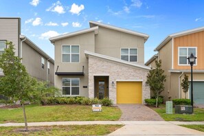 A modern two-story residential building with a stone facade, a yellow garage door, and a well-maintained lawn. - Storey Lake 5BR Themed Villa 10 min to Disney (Kissimmee)