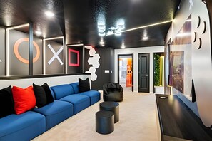 Un hall d’entrée moderne avec un canapé bleu, des coussins noirs et rouges, et un fauteuil noir. On y trouve deux tabourets noirs cylindriques et une table en bois. Les murs sont orn és d’œuvres d’art abstraites et d’un grand logo circulaire.
