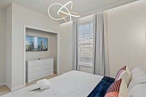 A modern bedroom with a large bed, a TV mounted on a wall, and a window with blinds. - Luxury 5BR Villa at Windsor Island Resort (Davenport)